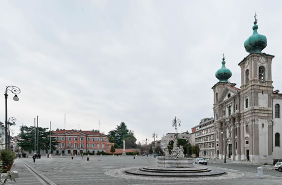 Piazza della Vittoria,  la settecentesca chiesa  di Sant’Ignazio a Gorizia  con i caratteristici coronamenti a cipolla  dei suoi campanili  e la fontana del Nettuno progettata da Nicolò Pacassi. 